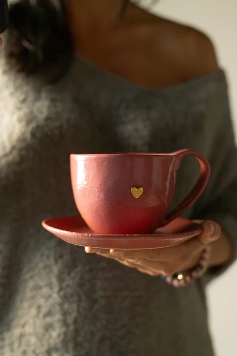 Malinowy kubek ceramiczny 400 ml handmade z talerzykiem, widok z boku, trzymany w dłoni
