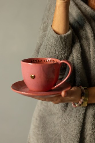 Kubek ceramiczny 400 ml malinowy handmade z talerzykiem, trzymany w dłoni