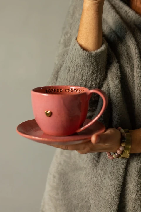 Kubek ceramiczny 400 ml malinowy handmade z talerzykiem, trzymany w dłoni