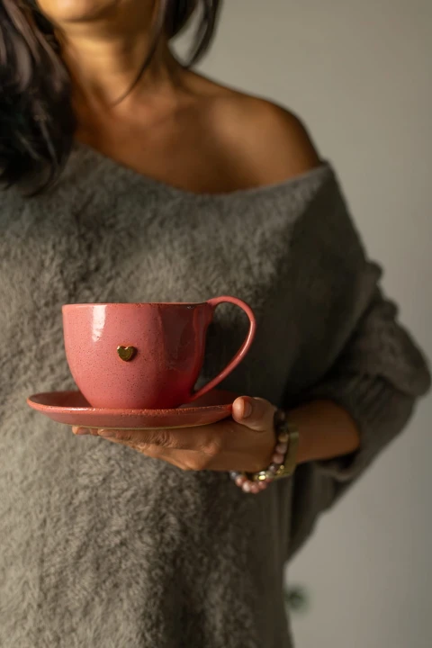 Ręcznie robiony kubek ceramiczny 400 ml w kolorze malinowym z talerzykiem, trzymany w dłoni