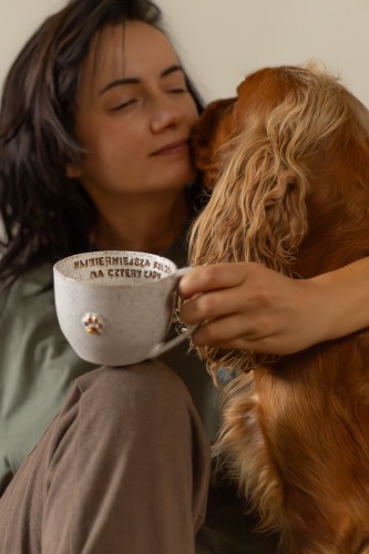 Duży kubek ceramiczny 400 ml ze złotą łapką i afirmacją stracciatella trzymany w dłoni kobiety przytulającej psa